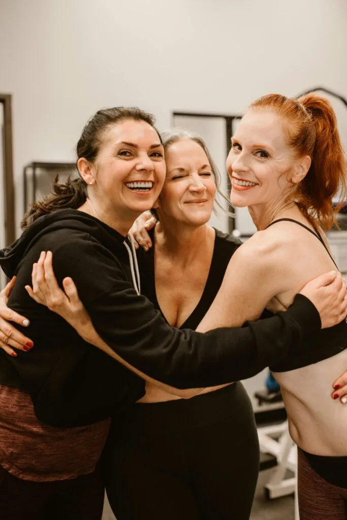 Three happy women hugging at the gym, celebrating friendship and wellness.
